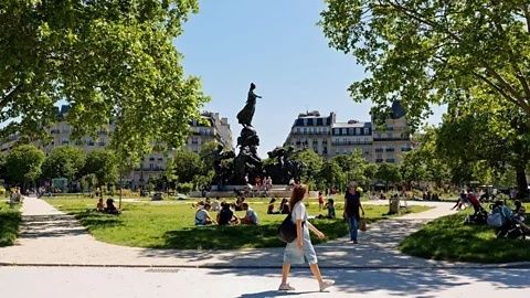 People walking and relaxing in a leafy urban park near city buildings