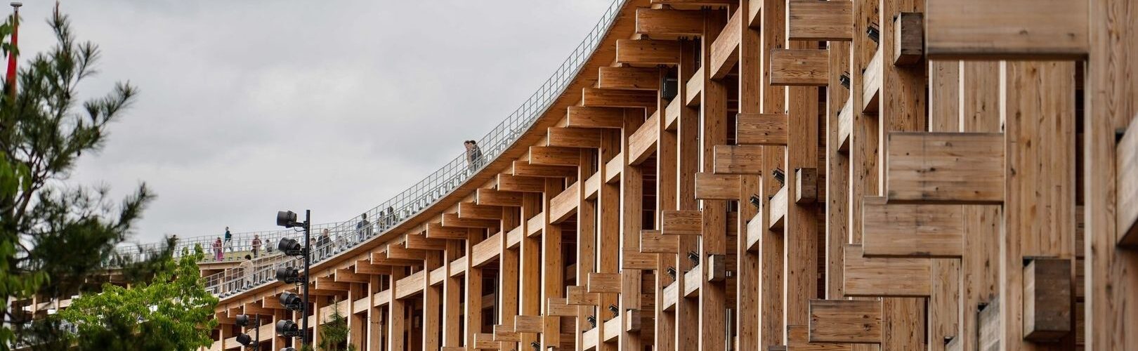 Large timber structure with repeated wooden beams under an overcast sky