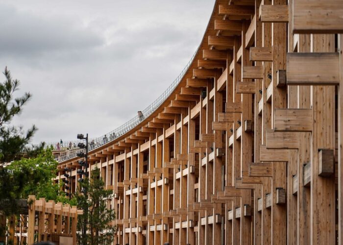 Large timber structure with repeated wooden beams under an overcast sky